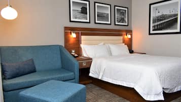 Habitación de hotel con una cama, un sofá azul y una mesita de noche. Hay cuadros enmarcados en la pared sobre la cama.