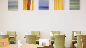 A dining area with green upholstered chairs, wooden tables, and abstract art on the wall.