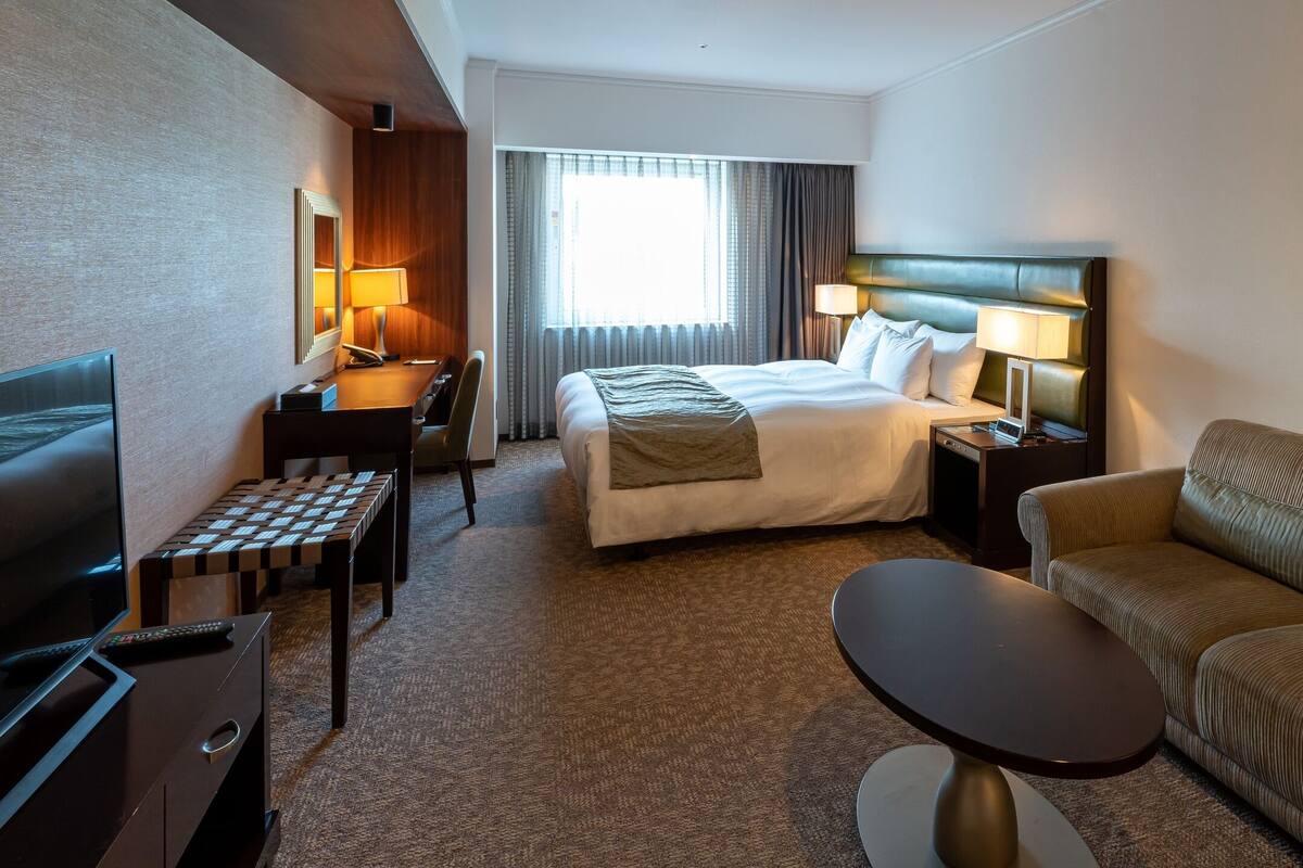 Una habitación de hotel con cama, sofá, televisión, escritorio y lámpara.