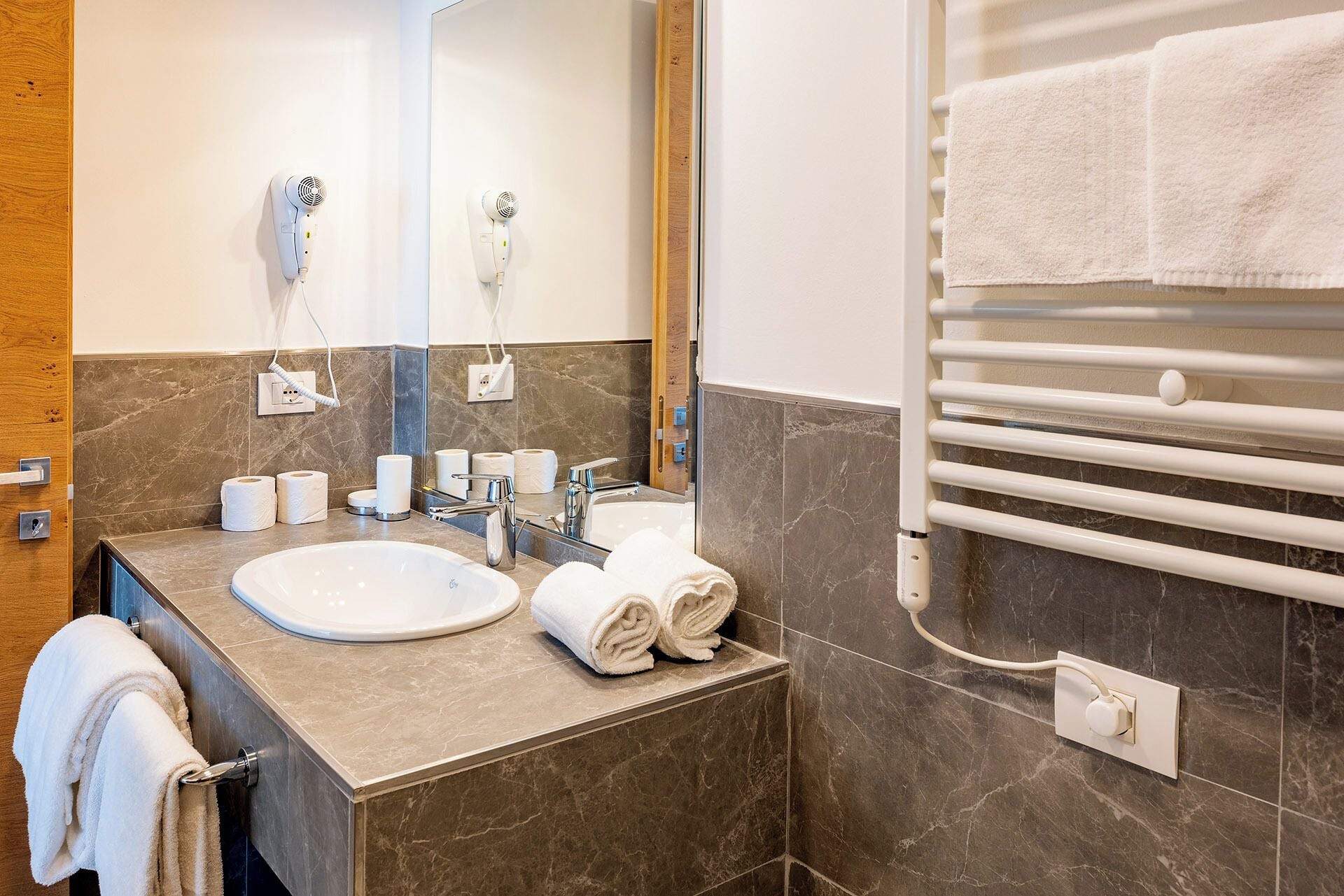A modern bathroom with a sink, mirror, towel rack, and marble tiles.