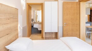 Una habitación de hotel moderna con cabecera de madera, una cama grande con ropa blanca, un armario de madera y un baño con espejo y lavabo.