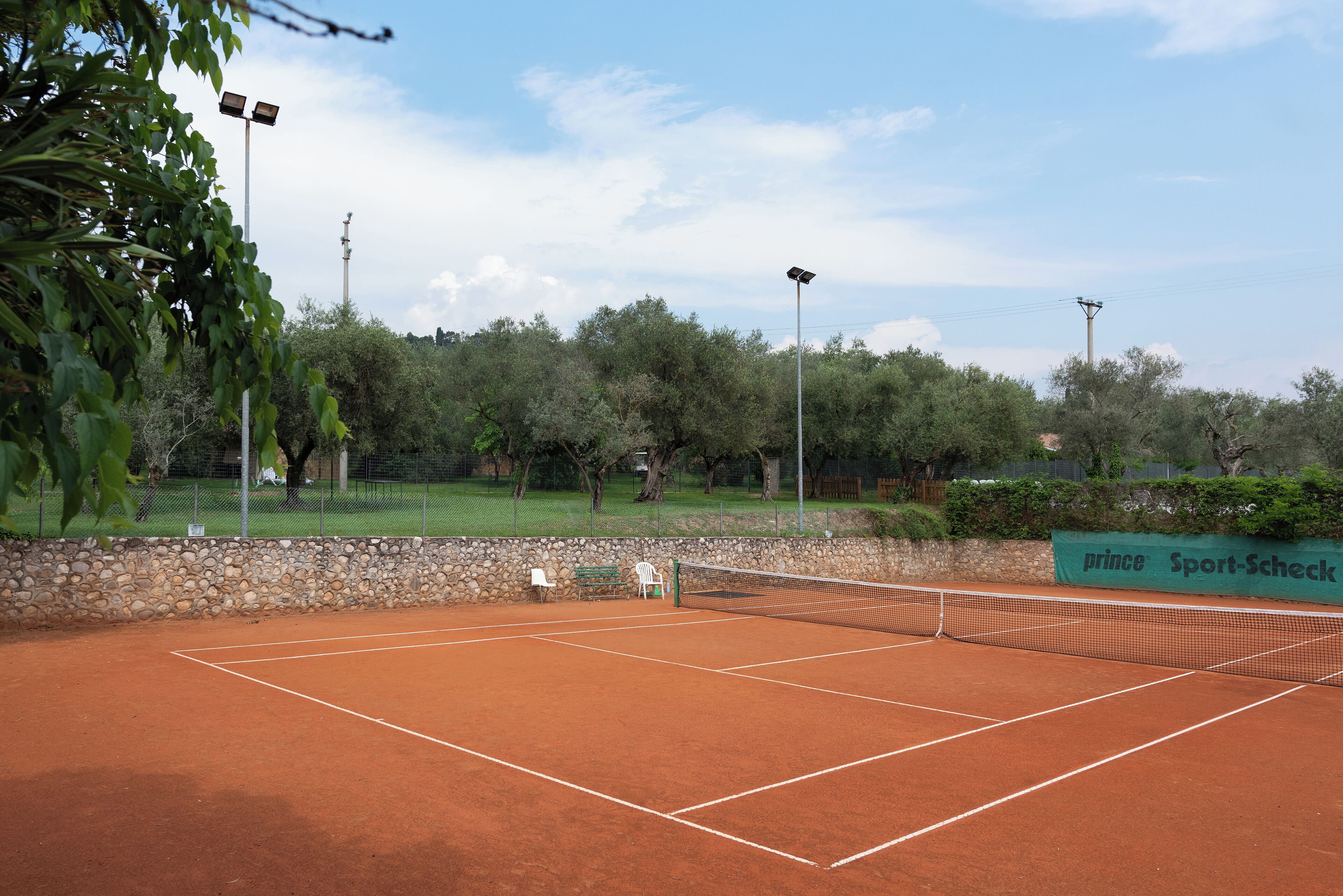 Una cancha de tenis con una red, rodeada de árboles y un muro de piedra.