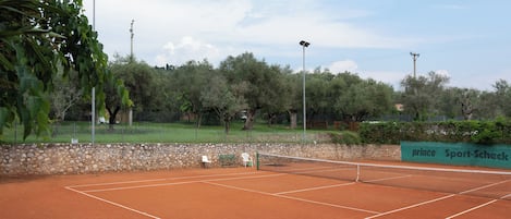A tennis court with a net, surrounded by trees and a stone wall.
