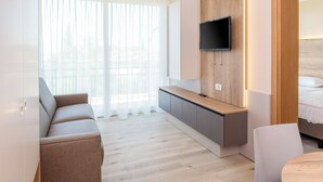 Una habitación de hotel moderna con sofá, una mesita, televisor montado en un panel de madera y una cama con cabecero.