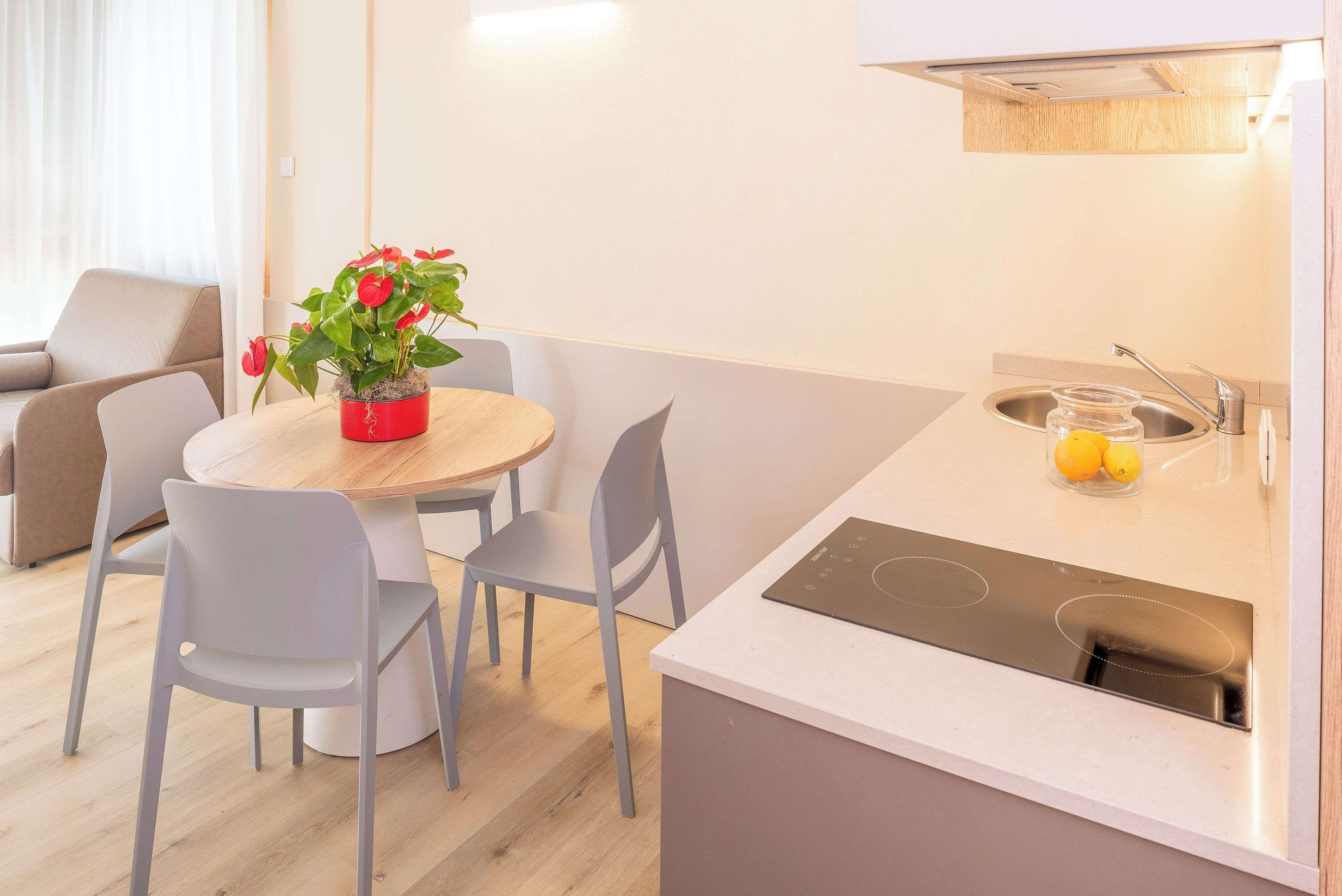 A modern kitchen with a round dining table, two chairs, a small island with a built-in stove, and a sink.