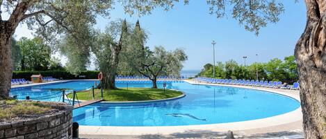 Une piscine bordée de pierres, entourée d’arbres et de chaises longues bleues.