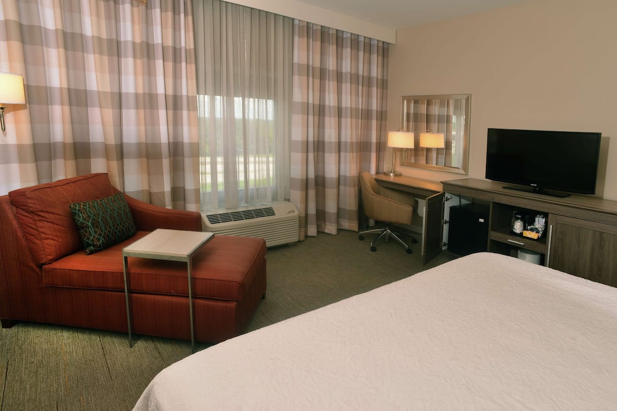 A hotel room with a bed, a desk, a chair, a television, and a window with curtains.