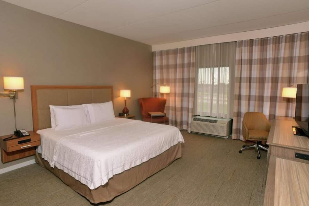 A hotel room with a large bed, two bedside lamps, a desk with a chair, and a window with curtains.