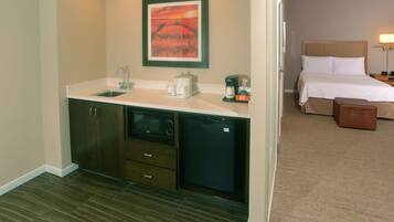 Una habitación de hotel con kitchenette, una cama, una mesita de noche y una maleta.