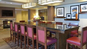 A hotel lobby with a large bar area, seating, a fireplace, and framed pictures on the walls. - Hampton Inn Springfield-Southeast (Springfield)