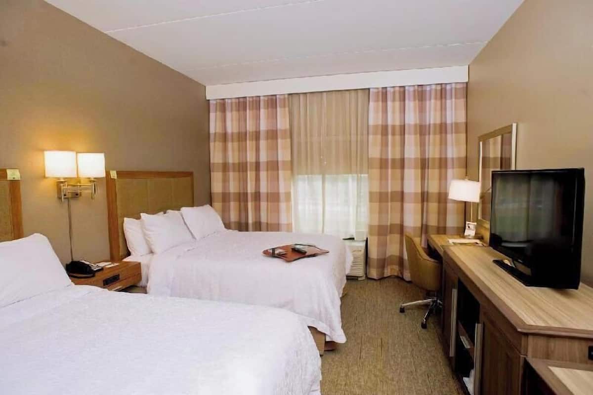 A hotel room with two beds, a desk with a TV, a lamp, and a window with curtains.