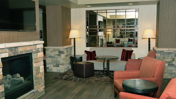 A cozy living room with a stone fireplace, comfortable seating, and a large mirror reflecting the room. - Hampton Inn Springfield-Southeast (Springfield)