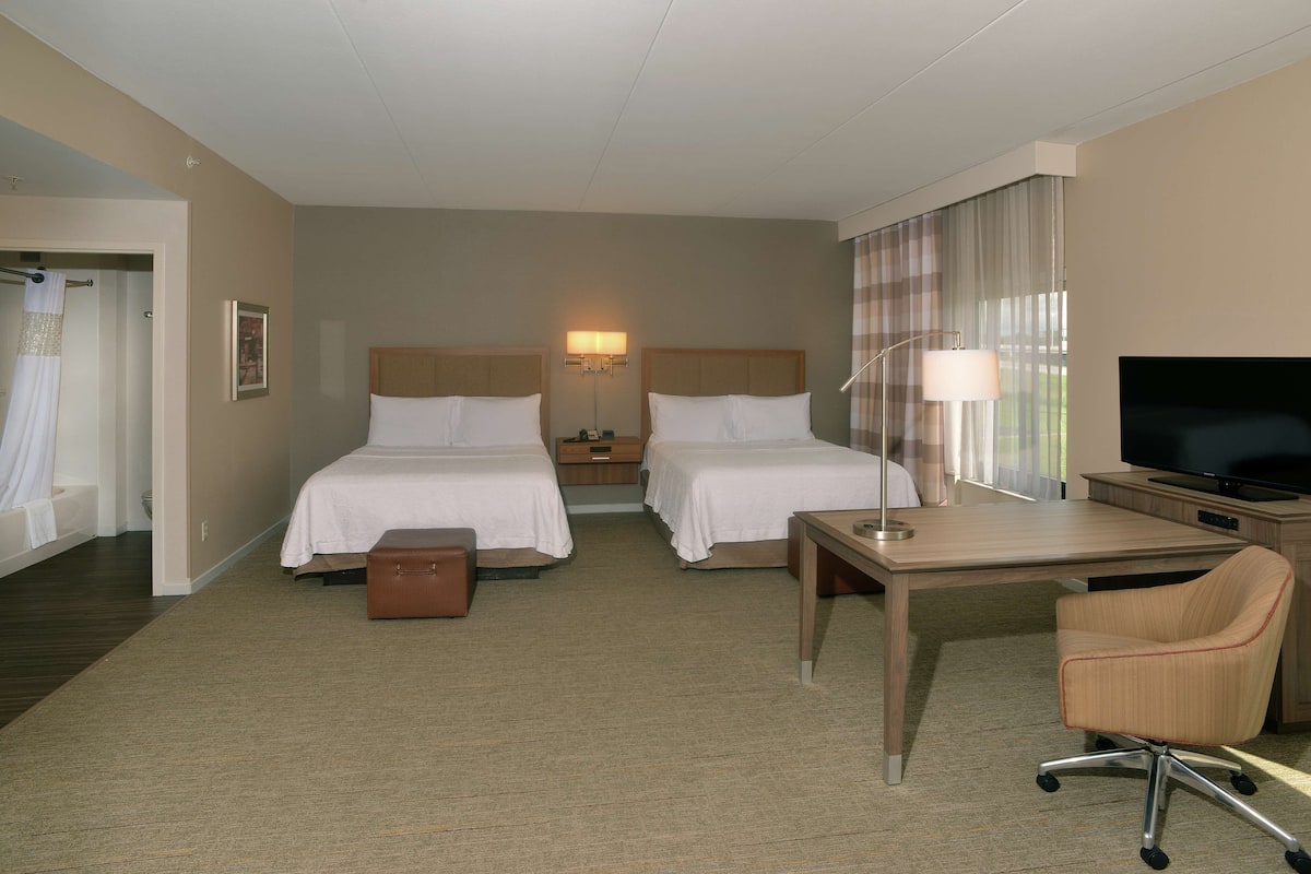 A hotel room with two beds, a desk, a chair, a television, and a bathroom.