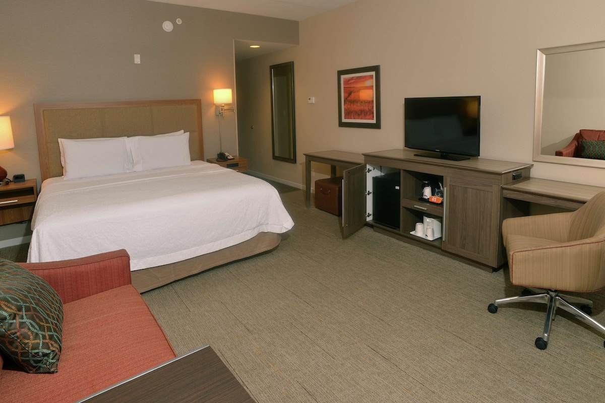 A hotel room with a bed, a desk with a television, a chair, and a mirror.
