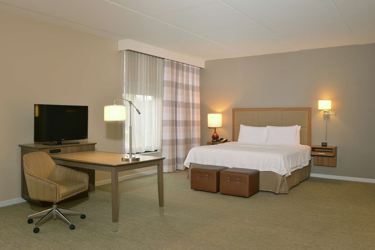 A hotel room with a bed, desk, chair, television, lamps, and a nightstand.