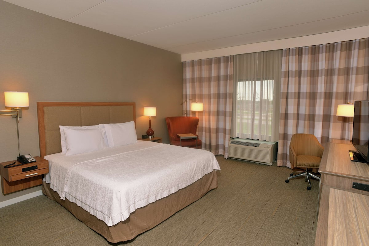 A hotel room with a large bed, two bedside lamps, a desk with a chair, and a window with curtains.