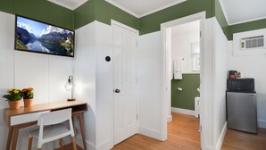 A compact room with a wooden desk, white chair, and a television mounted on the wall.