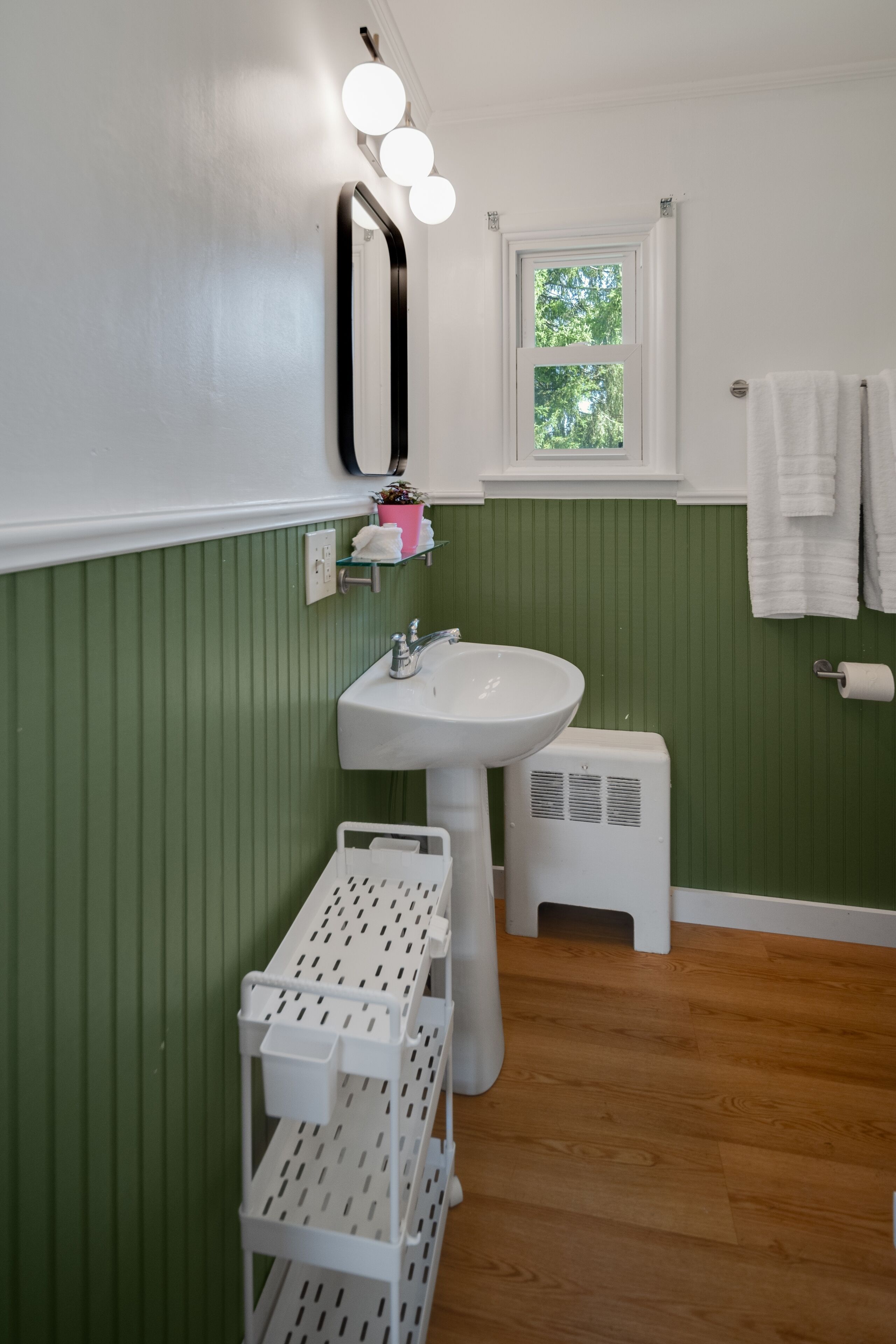 Un baño con un lavamanos blanco, paredes verdes, un espejo y una ventana.