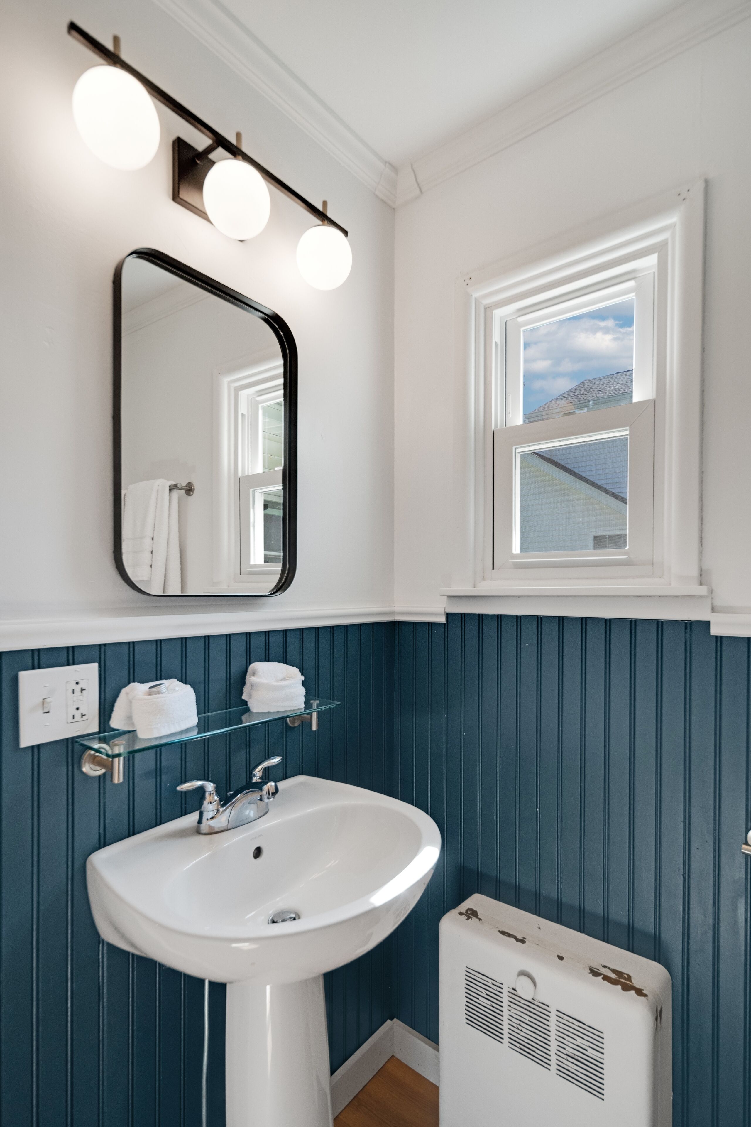 A bathroom with a white sink, a mirror, and a window with a view of the sky.