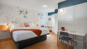 A modern bedroom with a bed, bedside table, lamp, and a desk with a chair.