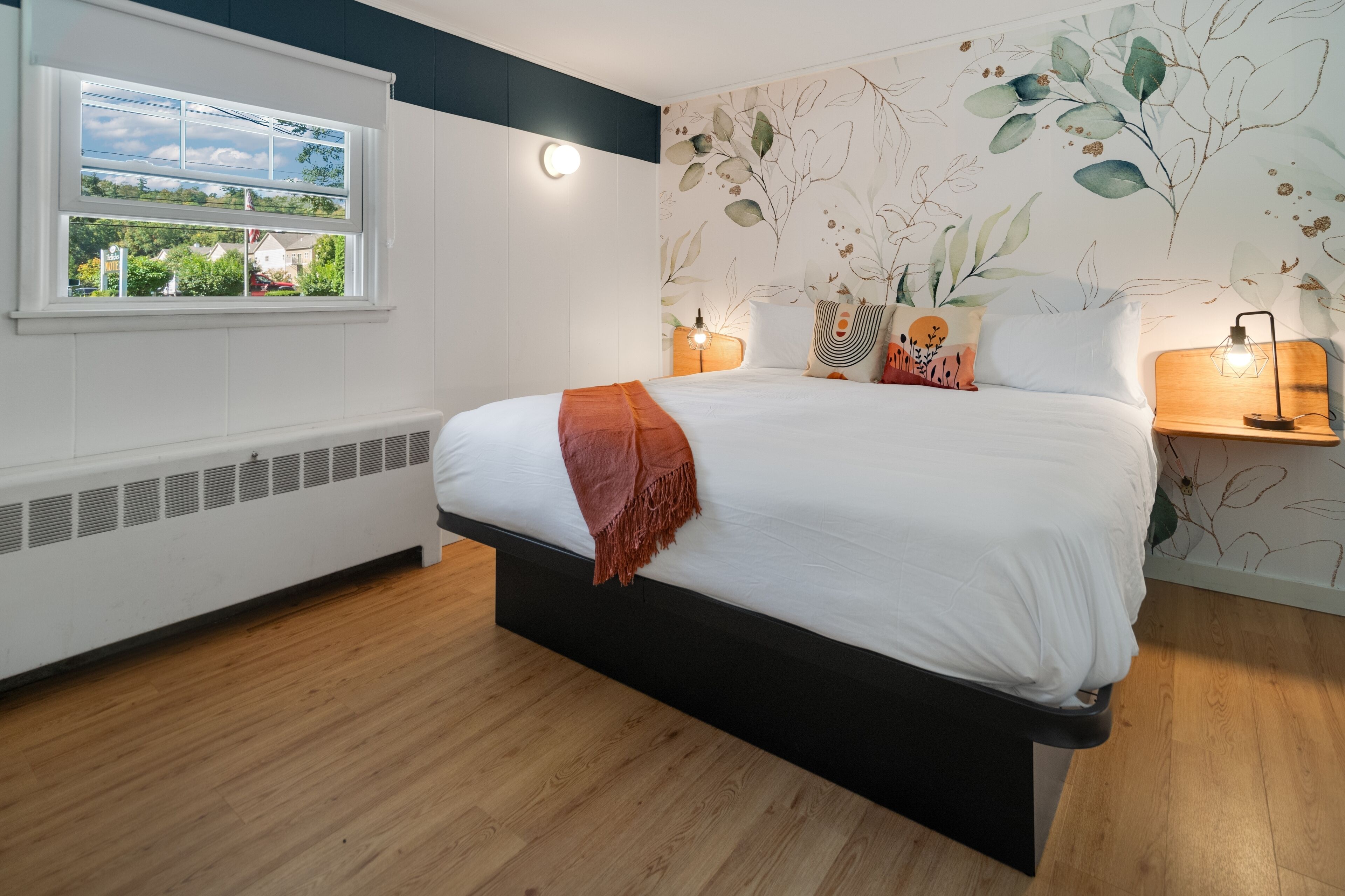 A bedroom with a bed, bedside lamps, a window with a view, and a wall with a leaf pattern.