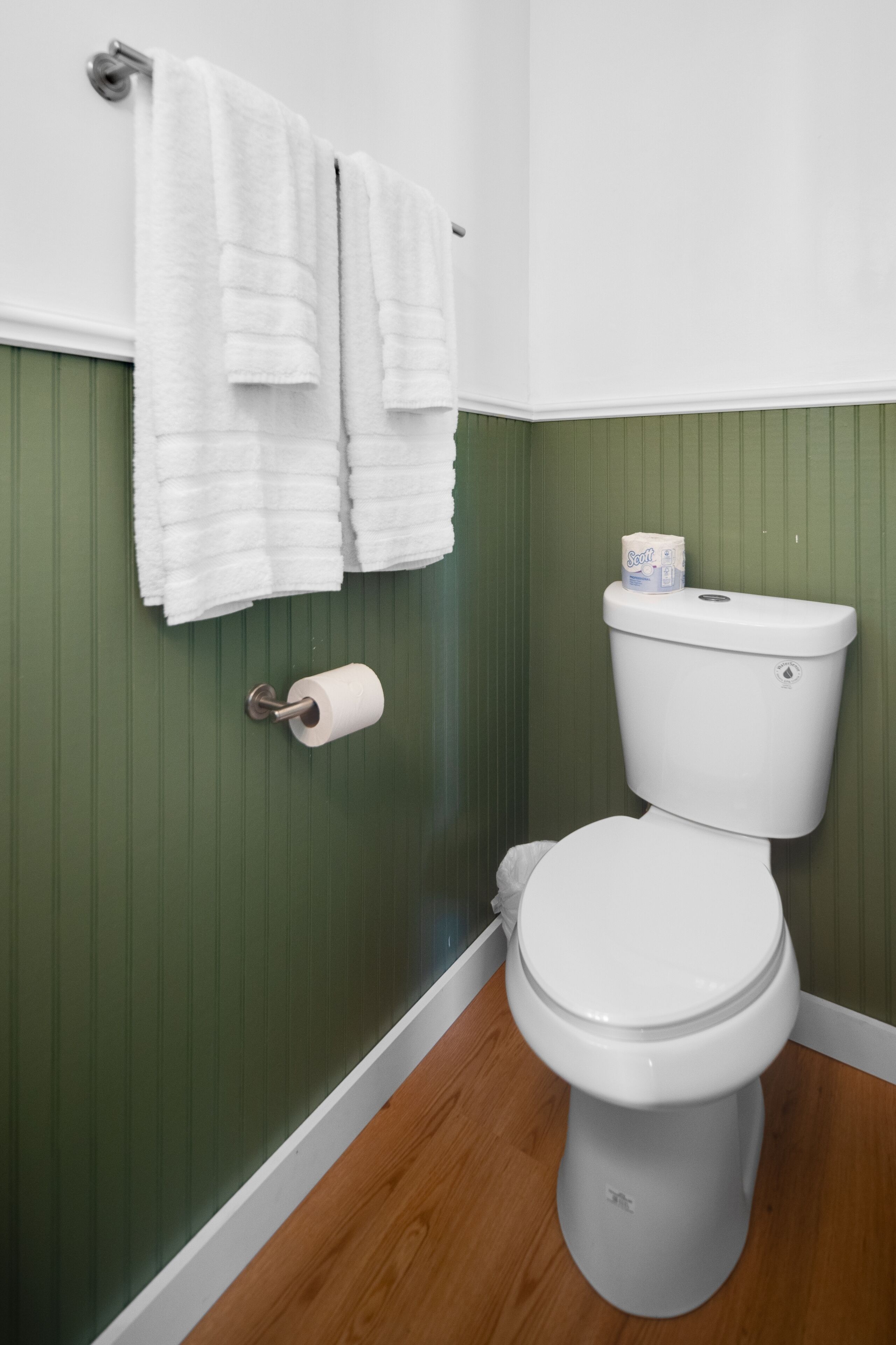 Un baño con inodoro blanco, paredes verdes y suelo de madera.