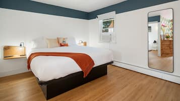Una camera da letto moderna con un letto, lampade da comodino, uno specchio grande e una finestra con un condizionatore.