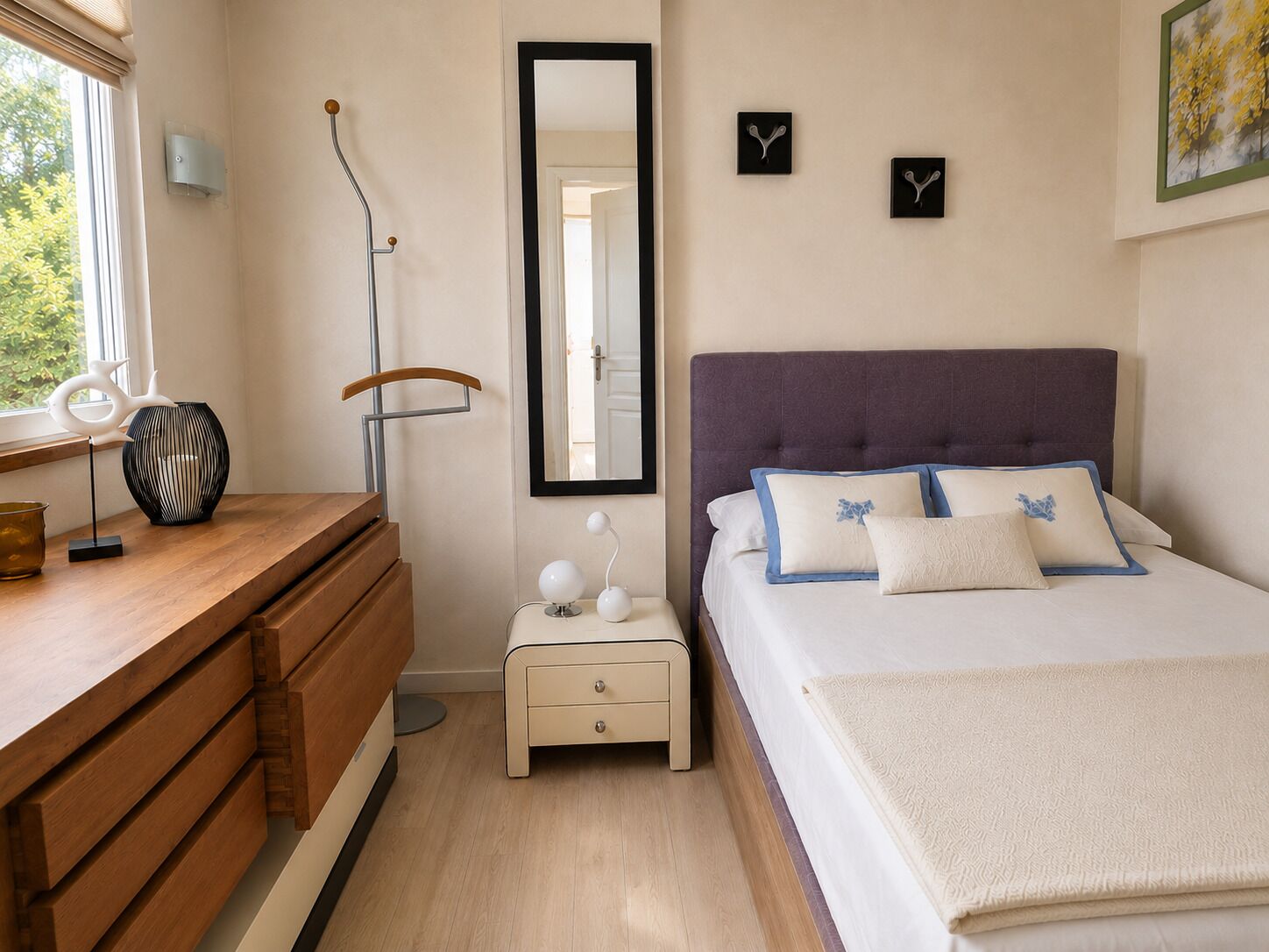 Ein Schlafzimmer mit Bett, Nachttisch, Kommode, Spiegel und Wanduhren.