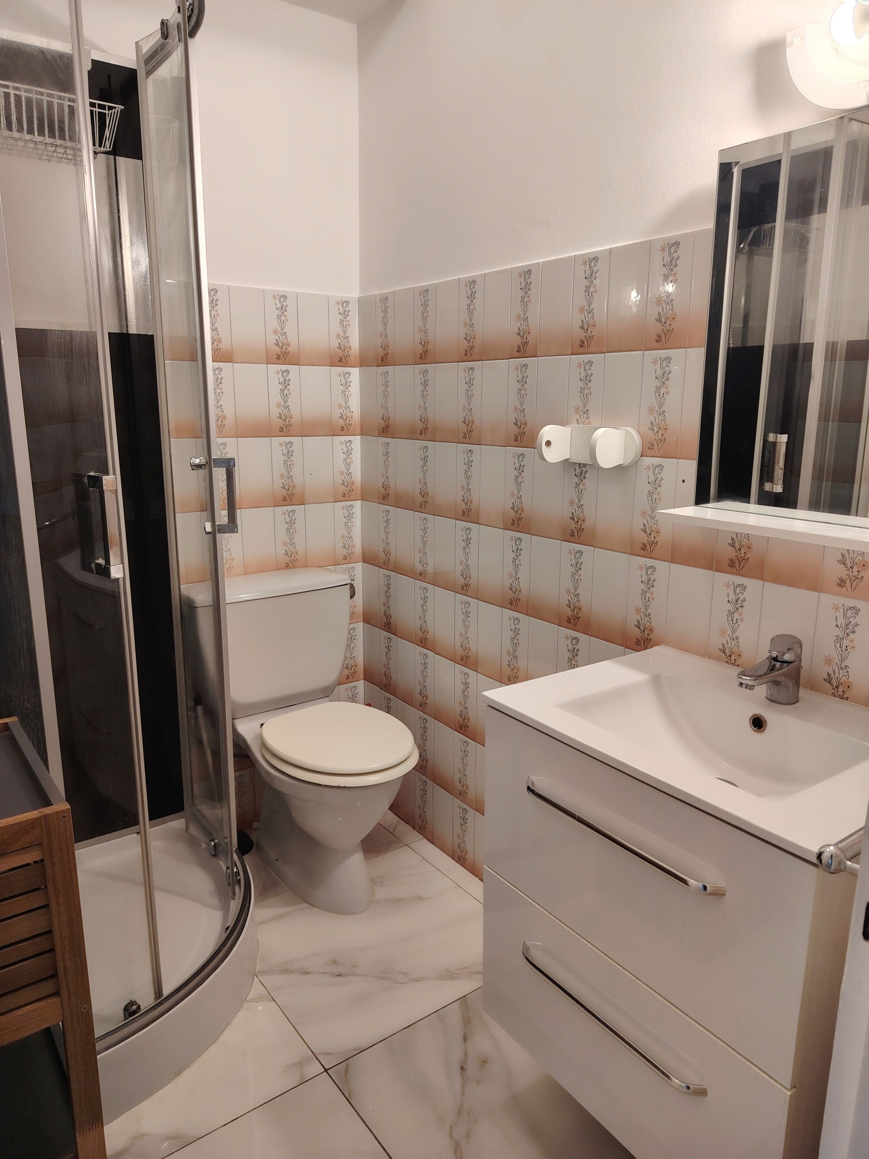 A bathroom with a toilet, a sink, a mirror, and a shower enclosure.