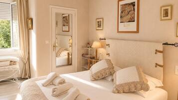 Habitación de hotel con cama, mesita de noche con lámpara, espejo y ventana con cortinas.