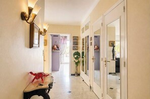 A hallway with a mirror, wall-mounted lights, a red sculpture, and a door leading to another room. - Sweet Accommodation (Cannes)