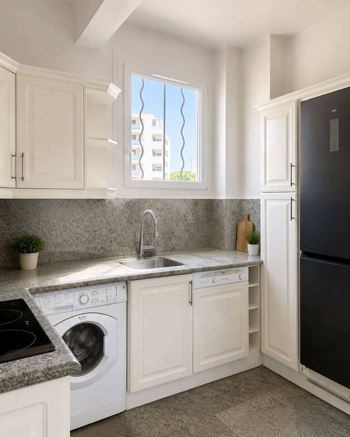 Cocina compacta con armarios blancos, lavadora integrada, pileta de acero inoxidable y refrigerador negro.