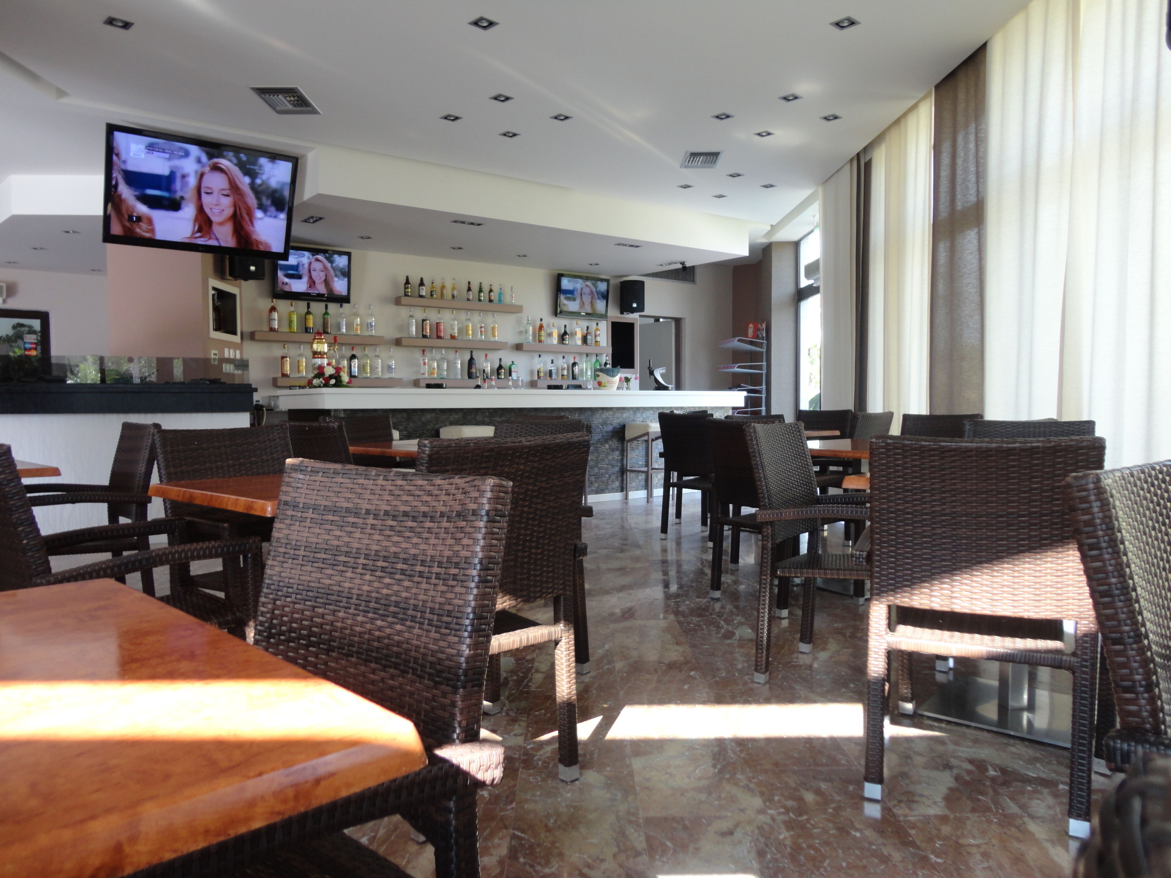 A restaurant with wicker furniture, a bar area with bottles, and a TV screen.