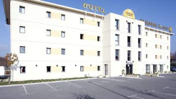 Un edificio de hotel con varios pisos, un estacionamiento al frente y un letrero que indica hotel Premier Class.