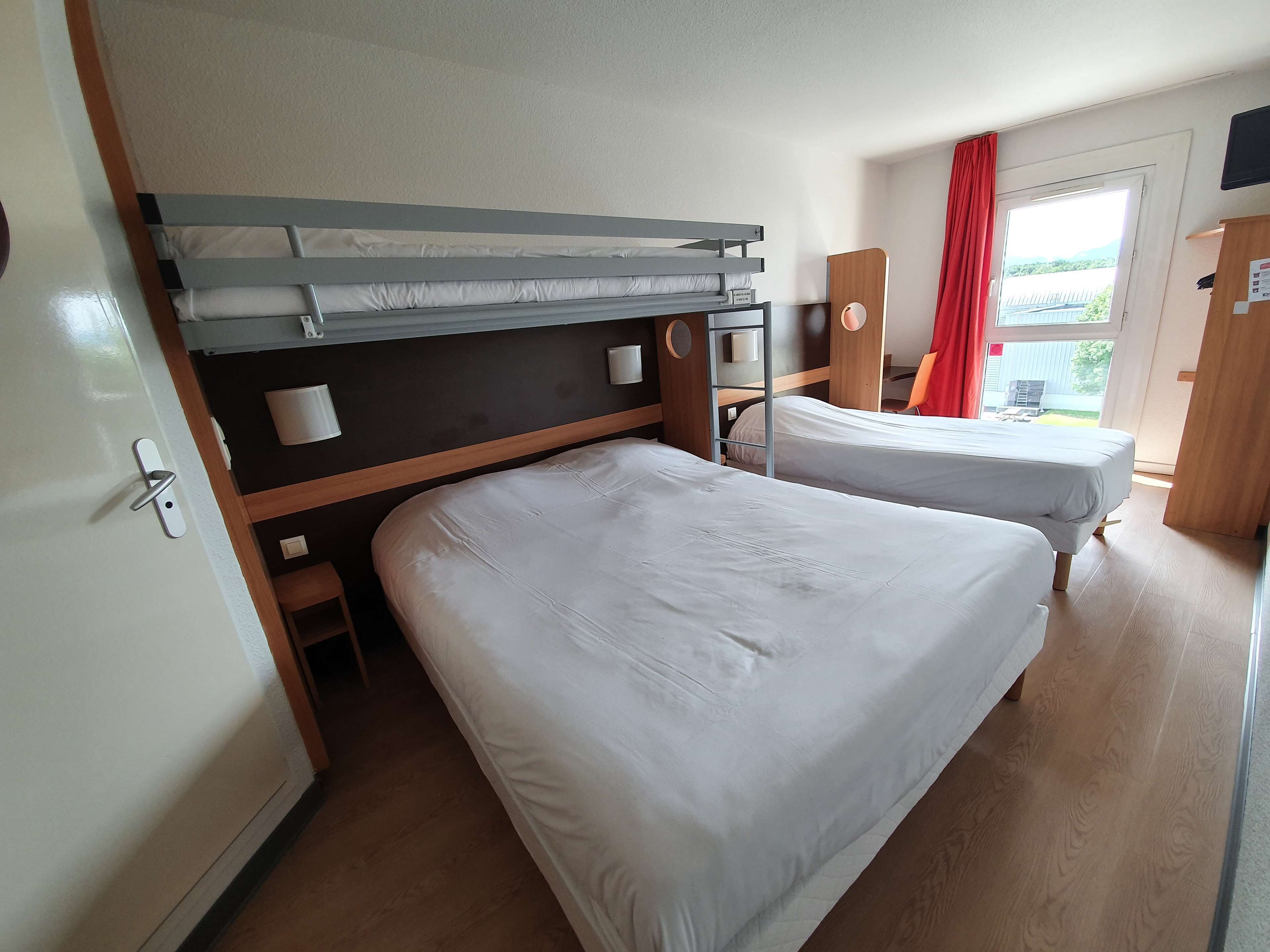 A hotel room with two beds, a wooden headboard, a small table, and a window with a view.