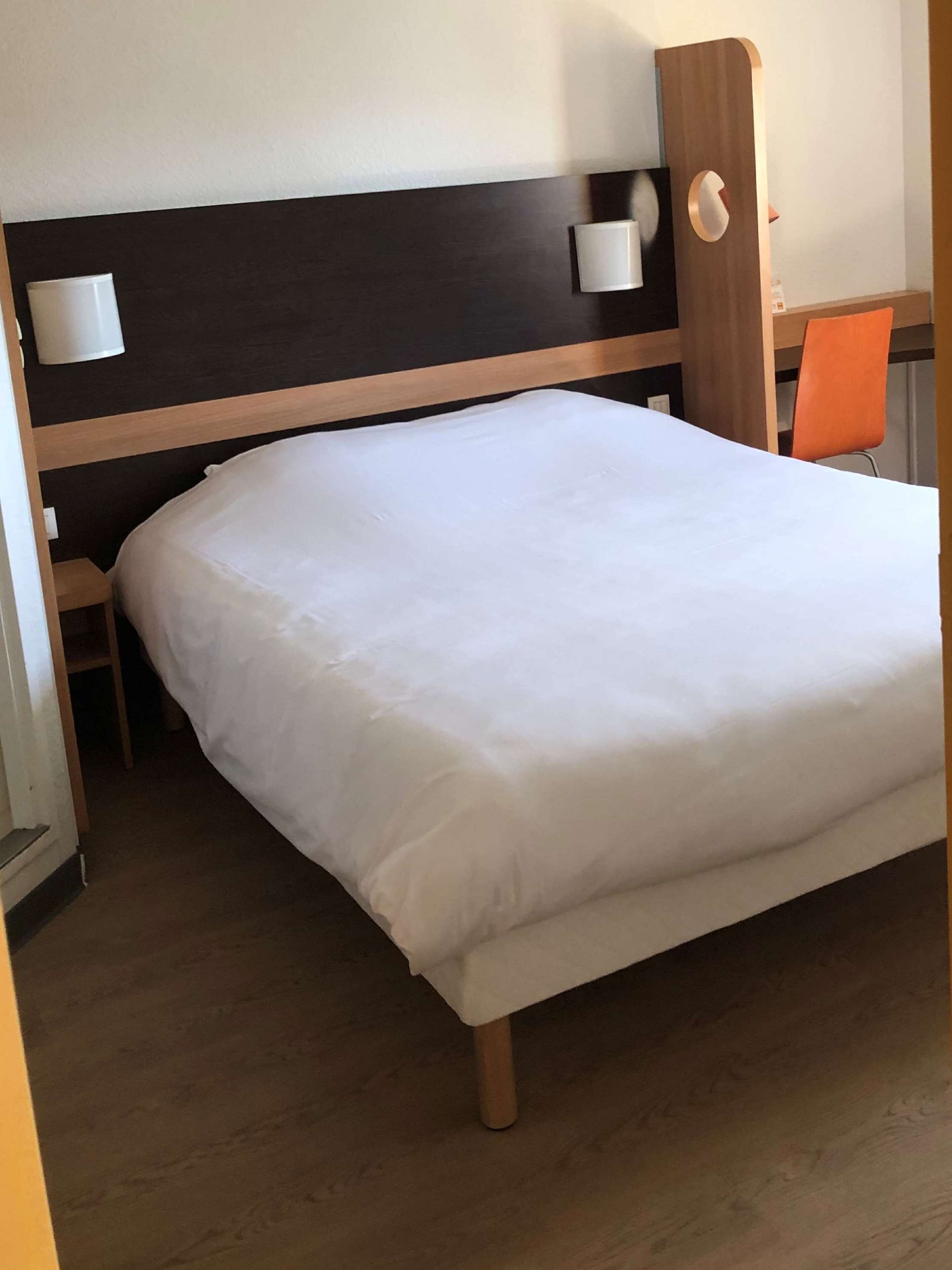 Una cama individual con cabecera de madera, una mesita de noche y una silla.
