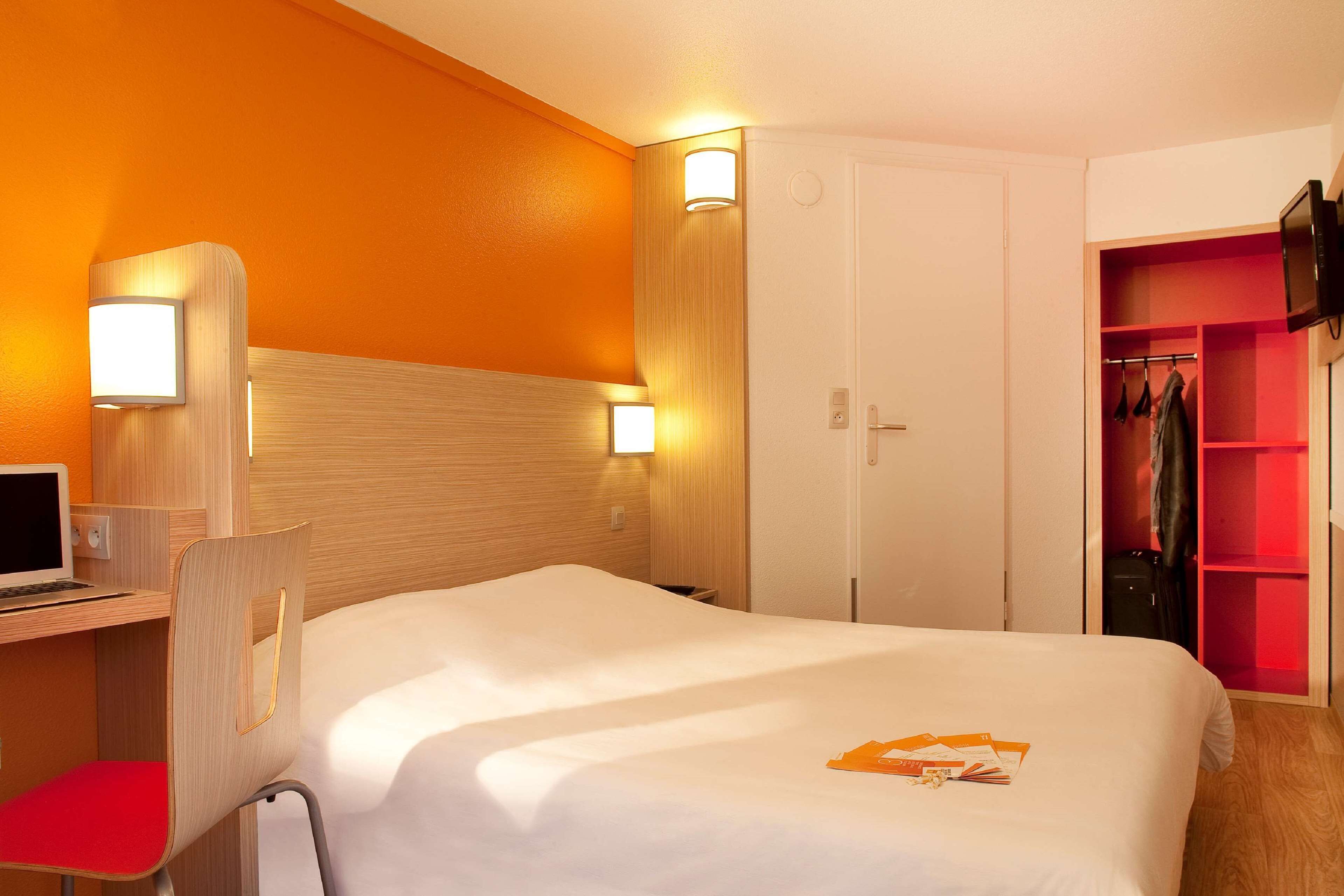 Une chambre d’hôtel comprenant un lit, un bureau avec un ordinateur, une chaise, une armoire et un téléviseur.