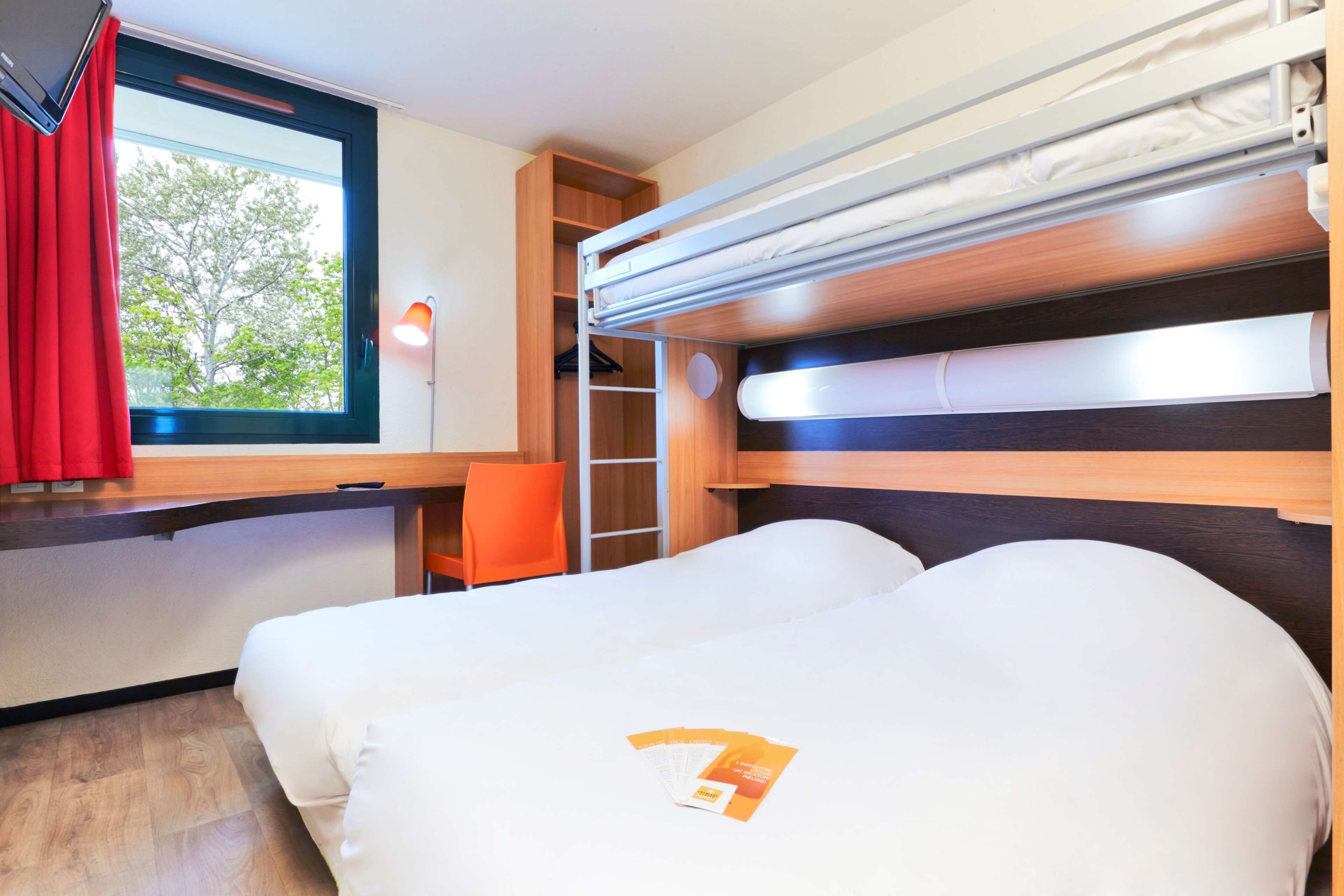 Una habitación pequeña con dos camas, un escritorio y una ventana con cortinas rojas.