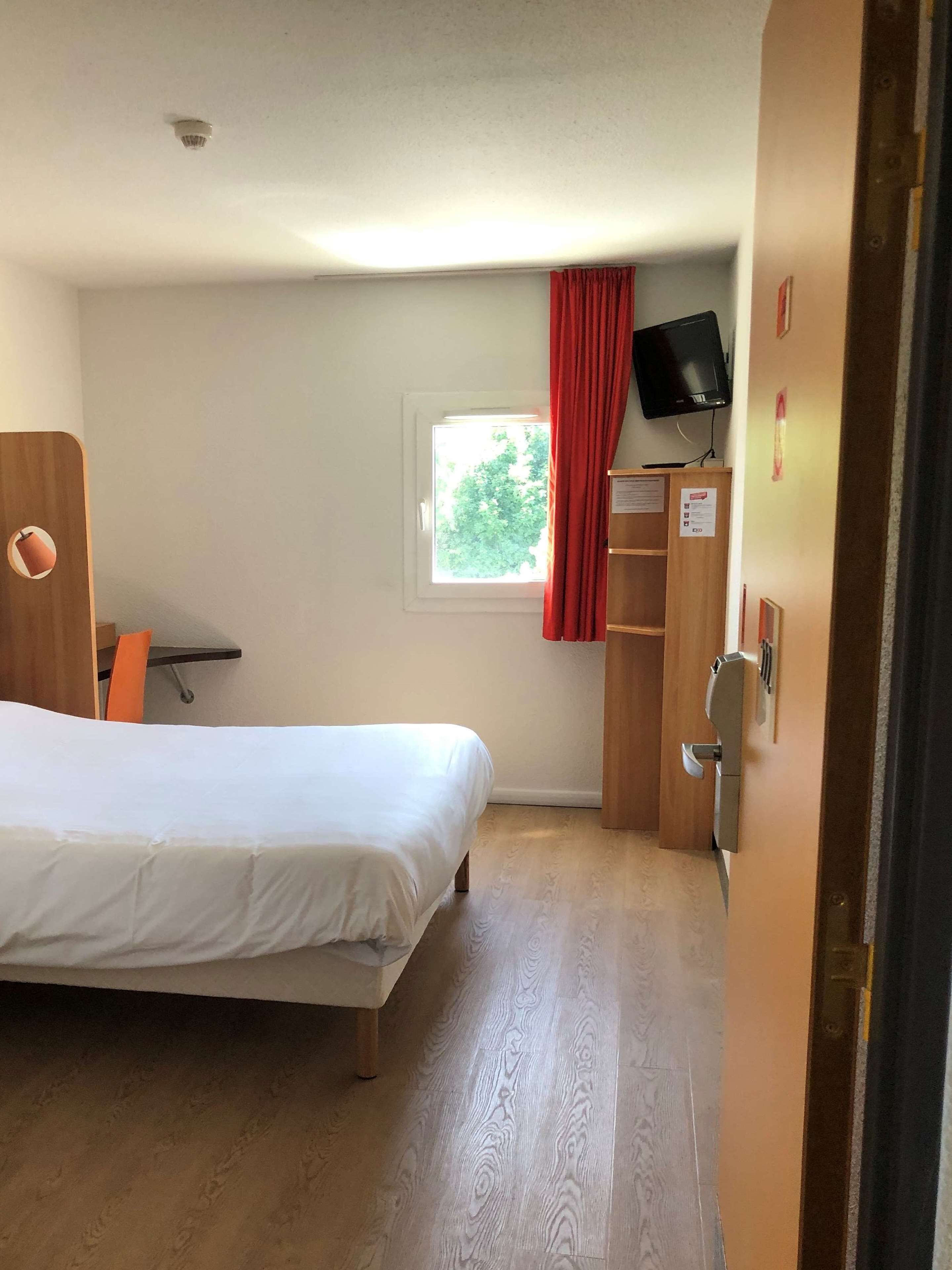 Habitació d'hotel amb llit, finestra amb cortines, televisió i armari de fusta.