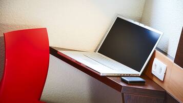 Un ordinateur portable sur un bureau, avec une chaise rouge, un téléphone et une prise électrique.