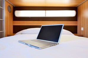A laptop on a bed with a wooden headboard and a window above. - Hotel Première Classe Annemasse - Ville La Grand (Ville-la-Grand)