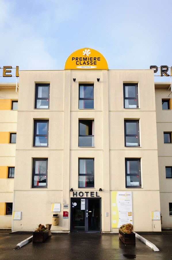 Fachada de hotel con un llamativo letrero amarillo que dice "PREMIERE CLASSE HOTELS" sobre la entrada.