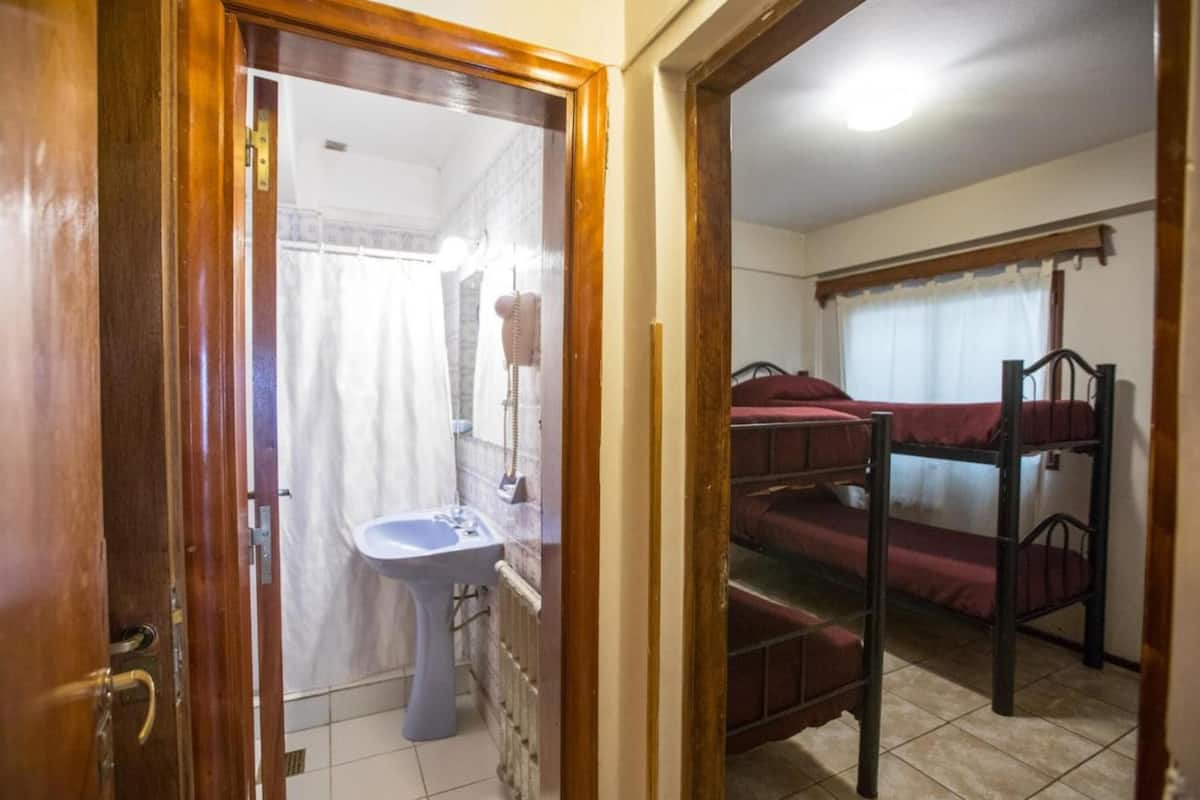 Una habitación con puerta de madera, lavamanos blanco y una cama litera con ropa de cama roja.