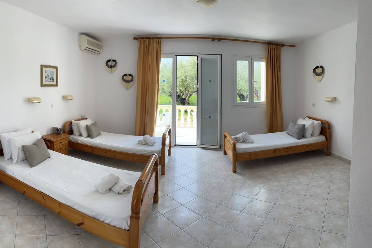 A room with three wooden beds, a bathroom with a sink, and a sliding glass door leading to an outdoor area.