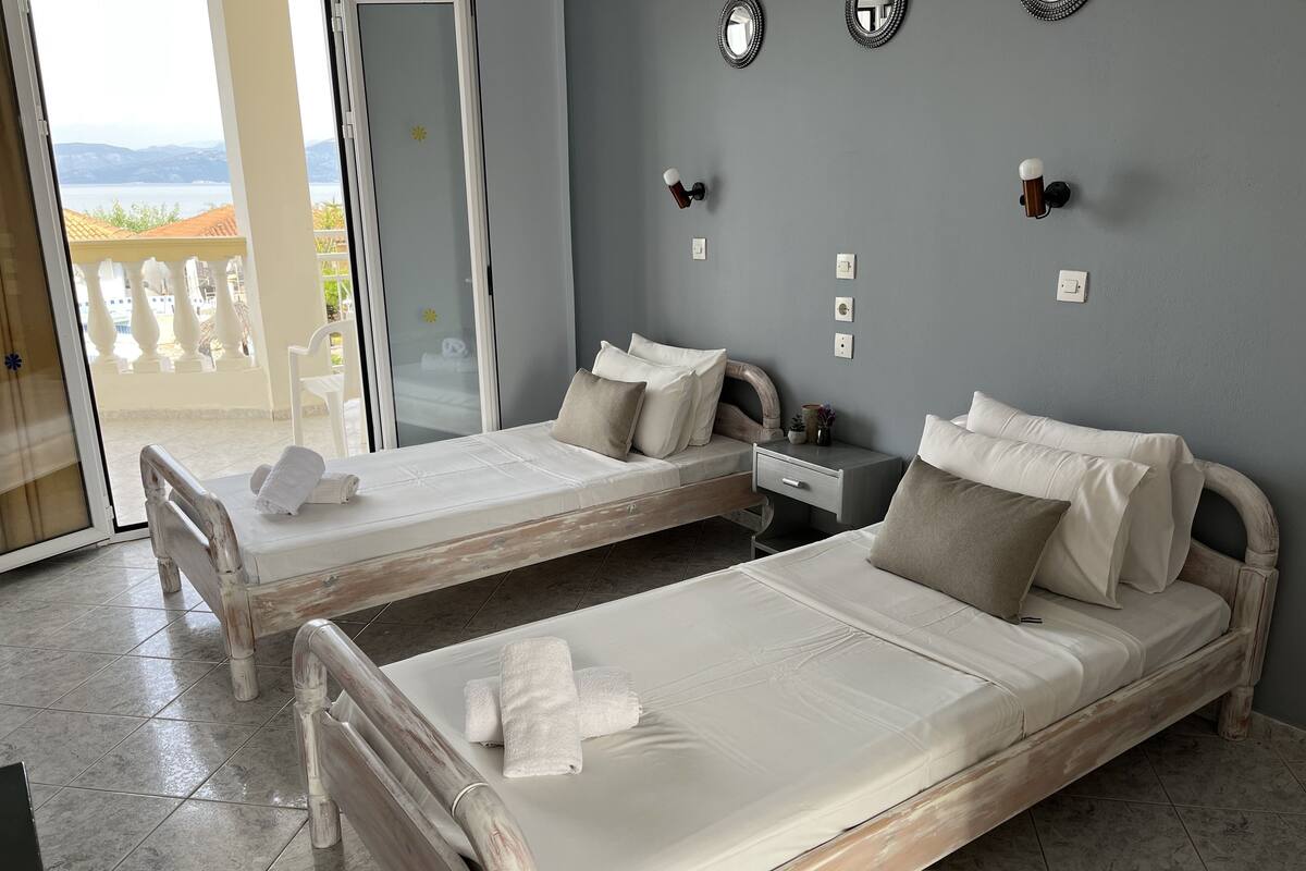 A hotel room with two beds, a small desk, and a view of the sea.
