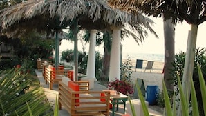 Un espace aménagé avec des bancs en bois et un toit de chaume, situé au bord de la plage et offrant une vue sur la mer.