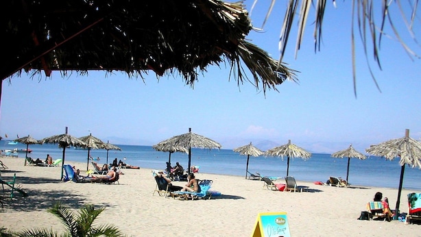Une plage avec des parasols en chaume, des chaises longues et des gens qui se détendent.