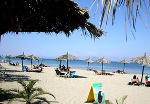 A beach with thatched umbrellas, lounge chairs, and people relaxing. - Sweet Dreams Apartments (Corfu)