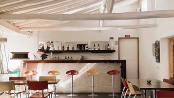 A modern bar area with a counter, stools, and a seating area with tables and chairs.