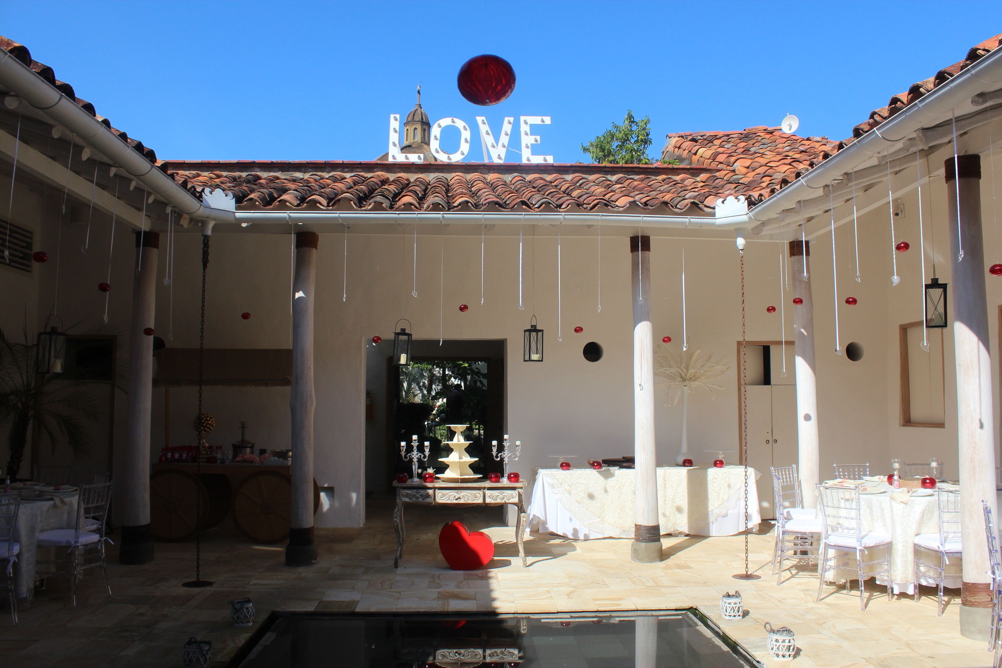 An outdoor patio area with a clear view of a building's facade displaying the word "LOVE" and a red balloon. There are tables set for dining, chairs, and a decorative heart-shaped chair.